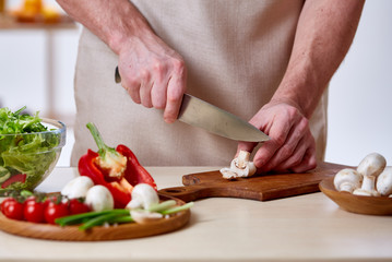 Man cooking at kitchen making healthy vegetable salad, close-up, selective focus.