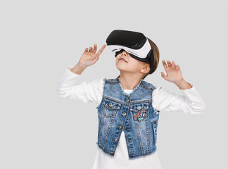 Little girl wearing virtual reality device over grey background. Hands up. Smartphone using with VR headset. Future gadgets technology concept