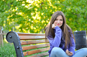 portrait of a young beautiful woman in a purple sports blazer that sits on a bench in the park and smiles