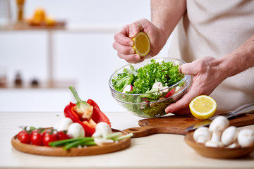 Man cooking at kitchen making healthy vegetable salad, close-up, selective focus.