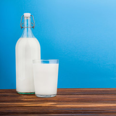 a glass of milk, a bottle of milk on a wooden table on a colored background