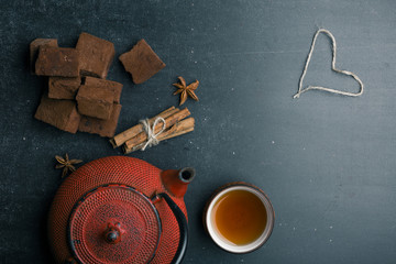 Tea composition with marshmallow, tea cup and traditional teapot on dark background.