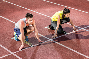 Male and female athlete in starting position at starting block of cinder track