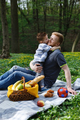 Cheerful dad and son have fun playing on the plaid in a green park