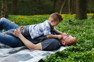 Naklejka na ściany i meble Cheerful dad and son have fun playing on the plaid in a green park