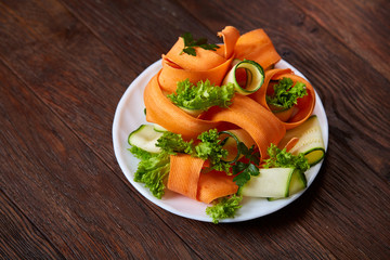 Artistically served vegetable salad with carrot, cucumber, letucce over wooden background, selective focus