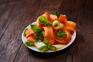 Artistically served vegetable salad with carrot, cucumber, letucce over wooden background, selective focus