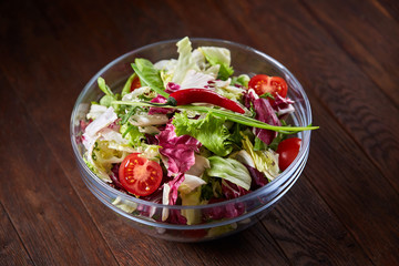 Fresh vegetable salad served in glass bowl over dark wooden background, selective focus, shallow depth of field