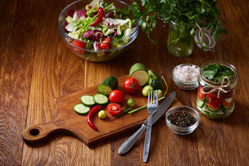 Delicious vegetable salad in jar and fresh veggies on cutting board on table, selective focus, close-up