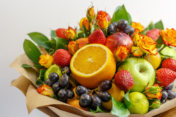 Bright bouquet consisting of apples, oranges, strawberries, grapes, plums and flowers of garden roses as a gift