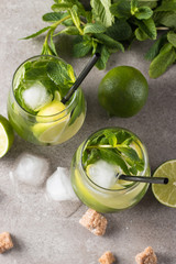 Fresh made mojito cocktail with lime, brown sugar, ice cubes and mint on a grey stone background. Alcoholic drink and lemonade concept.