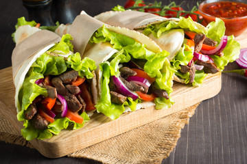 Photo of Mexican sandwich food, burrito, fajita, tacos, wrap made of tortilla, beef, chicken, fresh vegetables on rustic wooden background. Fast food concept. Healthy lunch snack. Copy space. 