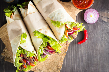 Photo of Mexican sandwich food, burrito, fajita, tacos, wrap made of tortilla, beef, chicken, fresh vegetables on rustic wooden background. Fast food concept. Healthy lunch snack. Copy space. 