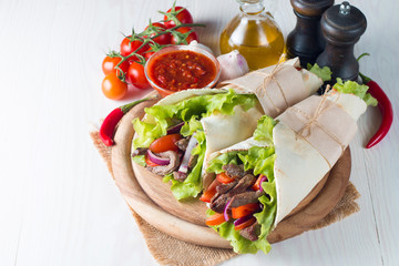 Photo of Mexican sandwich food, burrito, fajita, tacos, wrap made of tortilla, beef, chicken, fresh vegetables on rustic wooden background. Fast food concept. Healthy lunch snack. Copy space. 
