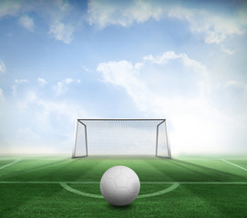 Digitally generated white leather football against football pitch and goal under blue sky