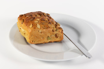 Kürbiskernbrötchen und Messer auf kleinem Teller isoliert auf weißem Hintergrund