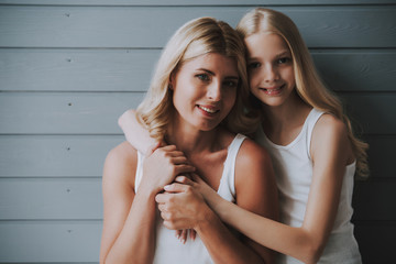 Blonde cute girl hugs blonde mother on wooden background.