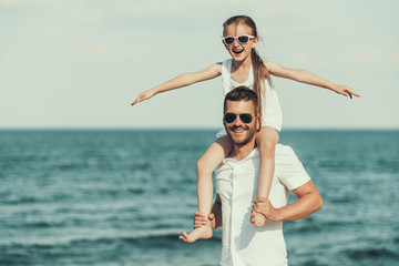 Little daughter in sunglasses sits on fathers neck.