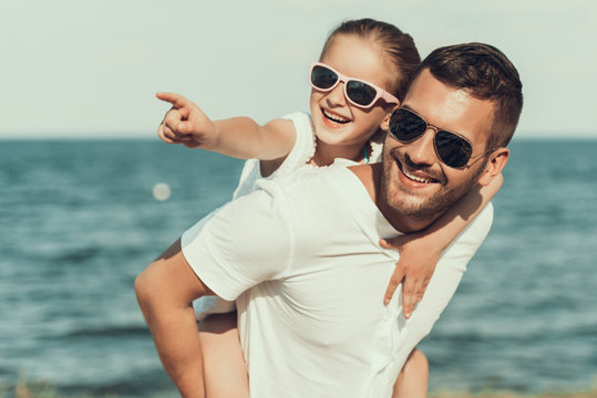 Happy little daughter in sunglasses sits on fathers back.