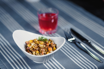 Table in the restaurant. On the table is a salad in a white plate, a knife, a fork, a glass with red juice. On the table is a blue tablecloth in strips.