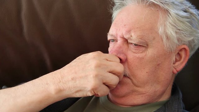 An older man rubs his irritated nose while lying on a sofa with room for text