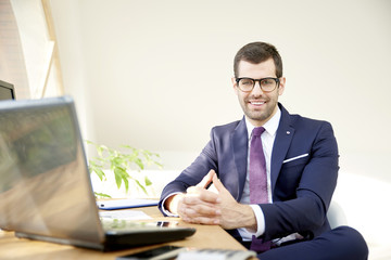 Businessman using laptop. Portrait of young financial assistant businessman wearing suit while sitting at office desk and working on financial report. 