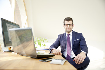Businessman using laptop. Portrait of young financial assistant businessman wearing suit while sitting at office desk and working on financial report. 