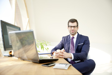 Businessman using laptop. Portrait of young financial assistant businessman wearing suit while sitting at office desk and working on financial report. 