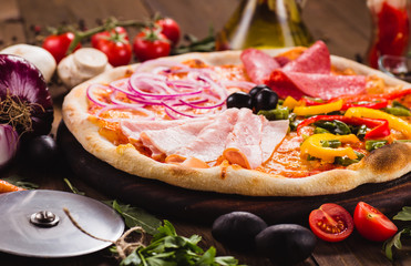 Italian Four Seasons Pizza (Quattro Stagioni) on the wooden background with ingredients around (close)