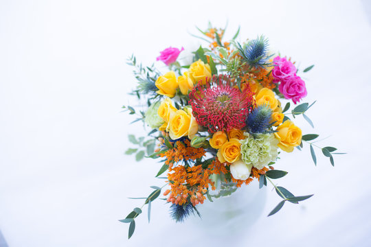 Colorful bouquet of yellow, coral and rose roses, blue eringium, red leucospermum, orange asclepia, eucalyptus and greenery