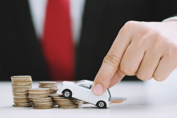 Business man in suit and red necktie  holding model of toy car on over a lot of stacked coins  - insurance, loan and buying car concept 