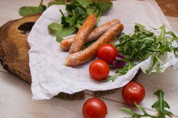 Grilled sausages with cherry tomatoes ,spinach and arugula on a wooden background in rustic style
