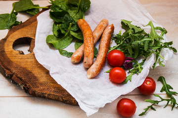 Grilled sausages with cherry tomatoes ,spinach and arugula on a wooden background in rustic style
