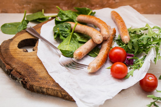 Grilled sausages with cherry tomatoes ,spinach and arugula on a wooden background in rustic style