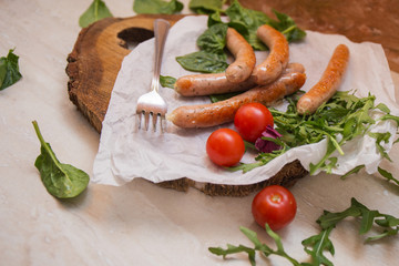Grilled sausages with cherry tomatoes ,spinach and arugula on a wooden background in rustic style