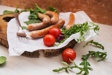 Grilled sausages with cherry tomatoes ,spinach and arugula on a wooden background in rustic style