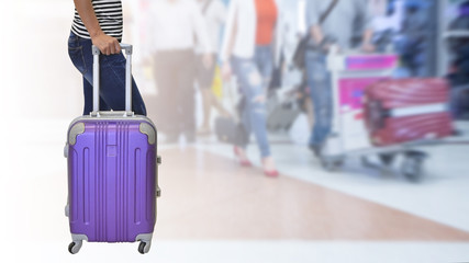 Female passenger was wearing jeans and a black and white shirt standing and holding her hand a purple suitcase with background airport , travel concept