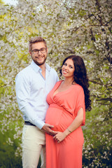 Obraz premium Romantic portrait of young smiling happy couple of lovely future parents during sunset on nature apple tree background in the city park. Pregnancy pregnant future mother photoshoot. Motherhood photo
