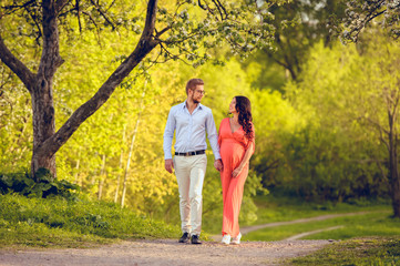 Fototapeta premium Romantic portrait of young smiling happy couple of lovely future parents during sunset on nature apple tree background in the city park. Pregnancy pregnant future mother photoshoot. Motherhood photo