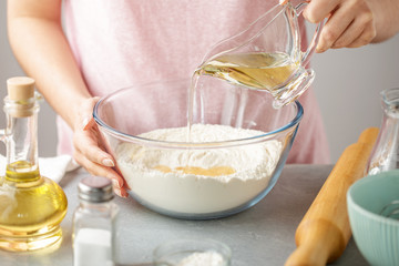 Female hands pour oil into bowl with flour, baking powder and salt. - 203117752