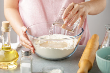 Woman pour hot water into bowl with flour, baking powder, salt and oil.