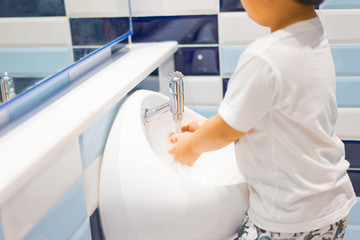 A boy is washing his hands himself. - Powered by Adobe