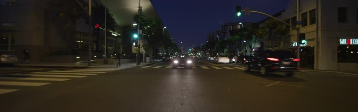 Rear view of a Driving Plate: Car travels on Santa Monica Boulevard in Santa Monica, California at dusk, crossing 6th Street and continuing to Ocean Avenue and turning right.