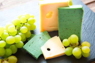 Various types of cheese with green grapes on black slate cheeseboard on table