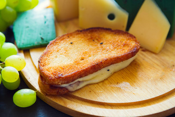 Hot grilled or fried sandwich with cheese and green grapes on black slate cheeseboard on wooden table