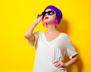 Young girl with pink hair in purple hat and sunglasses on yellow background