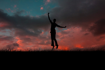 Obraz na płótnie Canvas Silhouette of jumping woman against red sky over grass