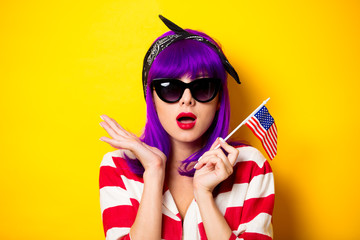 Young surprised girl with purple hair holding United States flag on yellow background. Fourth July...