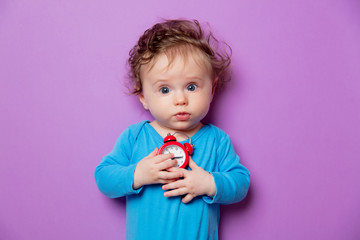 little infant baby with alarm clock lying on purple background