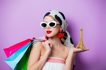 Portrait of beautiful style woman in sunglasses with Eiffel tower statue and shopping bags on purple background